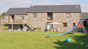 A stone house with a balcony, a slide, and a swing set in the yard. - 4 bedroom accommodation in Fairy Cross, Bideford (Fairy Cross, Bideford)