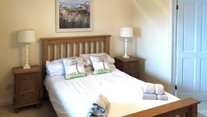 A bedroom with a wooden bed, two bedside tables with lamps, a painting on the wall, and a door. - 4 bedroom accommodation in Fairy Cross, Bideford (Fairy Cross, Bideford)