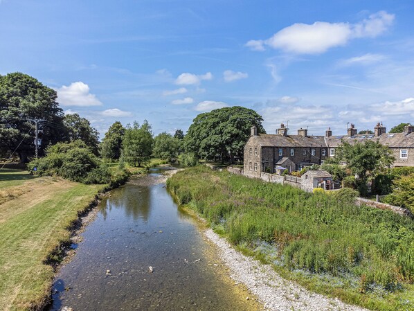 A river running through a rural area with stone buildings and lush greenery.