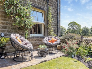 A stone building with two outdoor seating areas, a window, and a garden with various plants.