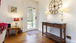A room with wooden flooring, a white door, a wall-mounted clock, two table lamps, a framed picture, and a small table with a red lamp. - 1 bedroom accommodation in Gargrave, near Skipton (Gargrave, near Skipton)