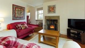 A living room with a fireplace, a red sofa, a wooden coffee table, and a television. - 1 bedroom accommodation in Gargrave, near Skipton (Gargrave, near Skipton)