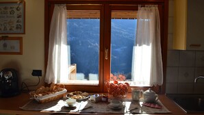 Una cocina con vistas a las montañas, una cafetera, una cesta de pan y una tetera sobre la encimera.