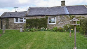 Une maison en pierre avec un toit en pente, un jardin fleuri et une mangeoire à oiseaux.