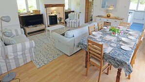 A spacious living area with a sofa, a dining table set for four, a fireplace, and a television. - Branscombe beach is only 1½ miles away and the Jurassic Coast is nearby. (Branscombe)