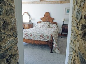 A bedroom with a wooden bed, floral bedding, a dresser, and a mirror.