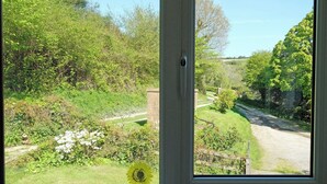 A window view of a garden with a pathway, greenery, and a clear sky. - Branscombe beach is only 1½ miles away and the Jurassic Coast is nearby. (Branscombe)