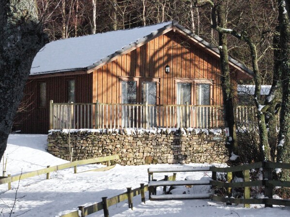 A wooden cabin with a stone foundation, a wooden porch, and a stone wall. - 3 bedroom accommodation in Greystoke, near Penrith (Greystoke, near Penrith)