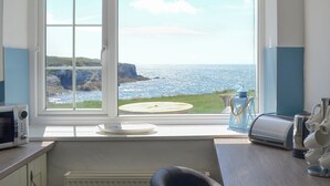 Une cuisine dotée d  ’une grande fenêtre donnant sur un paysage côtier, avec un four à micro-ondes, une bouilloire et une assiette posée sur le rebord de la fenêtre.