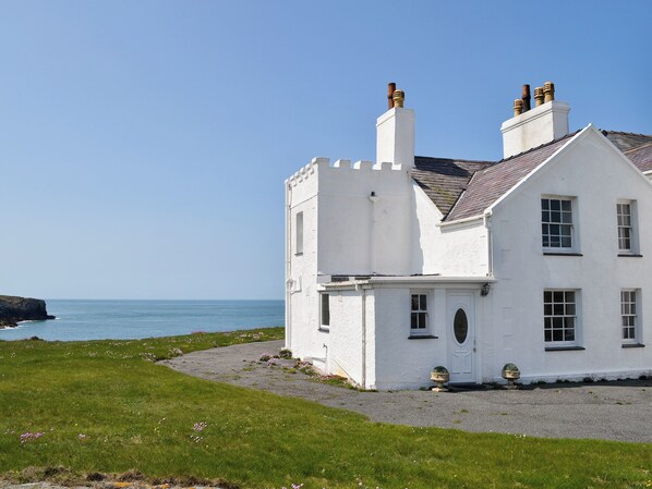 A white coastal house with a gravel driveway and a view of the sea. - 2 bedroom accommodation in Rhoscolyn, near Holyhead (Rhoscolyn, near Holyhead)