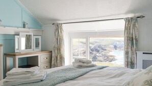 Une chambre à coucher avec un lit, une table de chevet, un miroir et une fenêtre avec des rideaux.