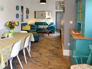 A living room with a sofa, a dining table with chairs, a coffee table, and a kitchen area with cabinets.