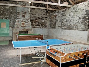 A room with a foosball table, ping pong table, and a stone wall with a wooden beam ceiling. - 8 bedroom accommodation in Colquite, Washaway (Colquite, Washaway)