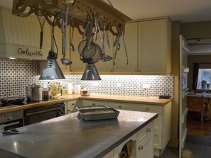 A kitchen with hanging utensils, a countertop with a baking dish, and a tiled backsplash.