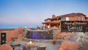 A luxurious outdoor patio with a stone waterfall, fire pit, and comfortable seating.
