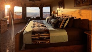 A bedroom with a large bed, a ceiling fan, and a view of a landscape through a window.