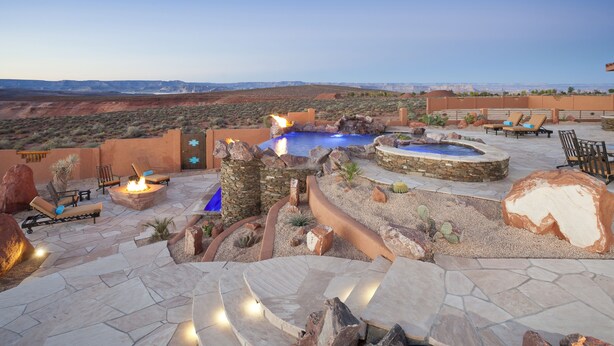 An outdoor patio with stone flooring, lounge chairs, a fire pit, and a small pool.