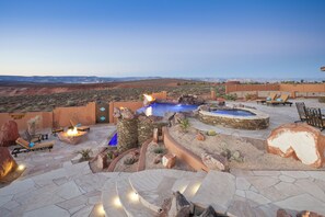Un patio exterior con suelo de piedra, sillones de descanso, un hogar para fuego y una pequeña piscina.