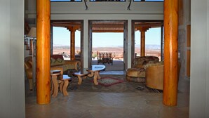 A spacious living area with a stone floor, wooden furniture, and a view of the desert landscape through large glass doors.