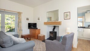 A living room with a sofa, a television, a fireplace, and a kitchen area visible through an open door. - Nettlebush Cottage-UK5629 (Drumelzier, near Peebles)