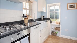 A modern kitchen with a gas stove, white cabinets, and a window with blinds. - Nettlebush Cottage-UK5629 (Drumelzier, near Peebles)