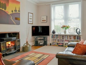A living room with a fireplace, a television, a bookshelf, and a window with blinds.