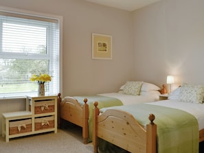 A bedroom with two beds, a bedside table, a lamp, and a window with blinds.