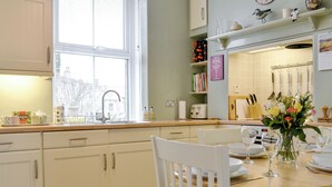 A kitchen with white cabinets, a window, a sink, and a dining table set for two with a vase of flowers.