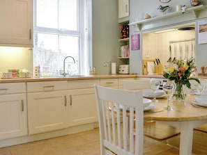A kitchen with white cabinets, a window, a sink, and a dining table set for two with a vase of flowers.