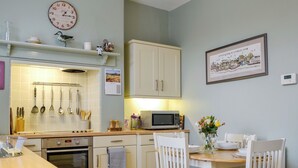 A kitchen with a microwave, oven, and various utensils. There is a dining table with chairs and a vase of flowers.