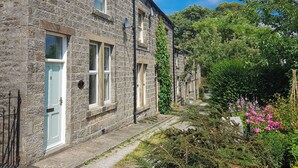 A stone building with a light blue door, a narrow pathway, and lush greenery.