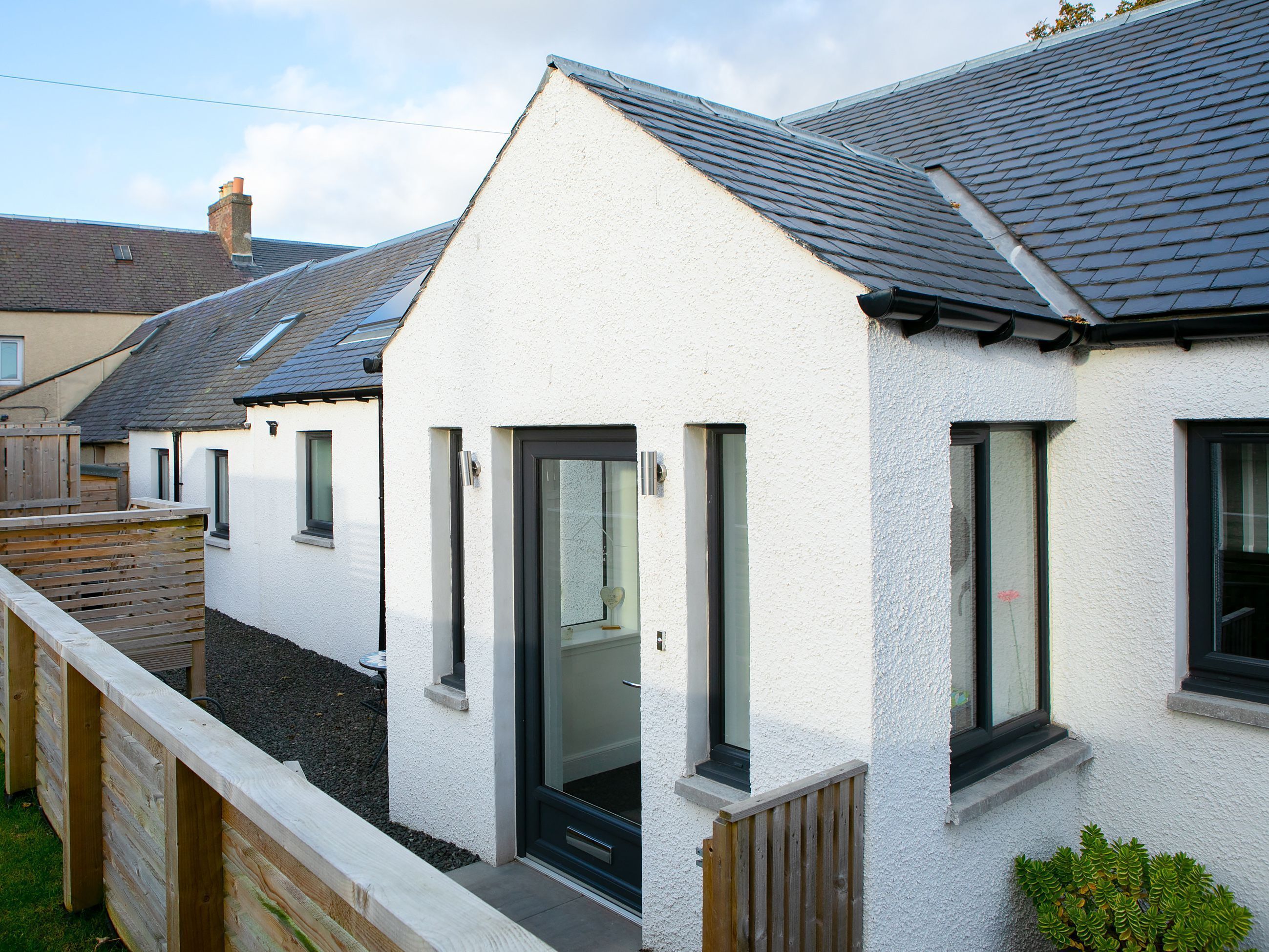 A row of modern white houses with grey roofs, wooden fences, and small windows.