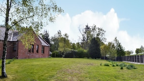Un bâtiment en briques doté d’un toit en pente, entouré d’une cour verdoyante et d’arbres.