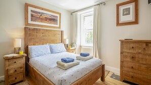 Une chambre à coucher avec un lit en bois, deux tables de chevet, une commode, une coiffeuse et une fenêtre avec des rideaux.