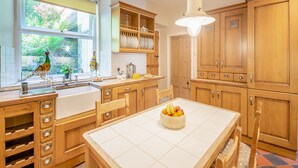 Une cuisine avec des meubles en bois, un plan de travail blanc, un évier et une table à manger agrémentée d’un panier de fruits.