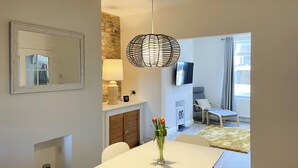 A modern living room with a white sofa, a TV mounted on the wall, and a dining area with a white table and chairs. - 2 bedroom accommodation in Amble, near Warkworth (Amble, near Warkworth)
