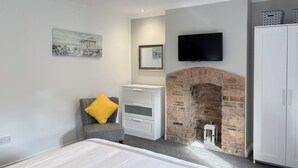 A bedroom with a bed, a gray armchair with a yellow pillow, a white dresser, a brick fireplace, a television mounted above the fireplace, and a wardrobe. - 2 bedroom accommodation in Amble, near Warkworth (Amble, near Warkworth)