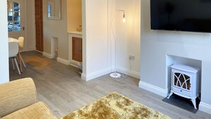 A living room with a TV, a fireplace, and a dining area with chairs and a table. - 2 bedroom accommodation in Amble, near Warkworth (Amble, near Warkworth)