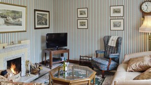 Un soggiorno con camino, televisore, una poltrona decorata e un divano.