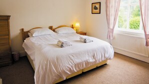 Un letto rifatto con cuscini e asciugamani piegati, una lampada da comodino, un quadro appeso alla parete e una finestra con tende.