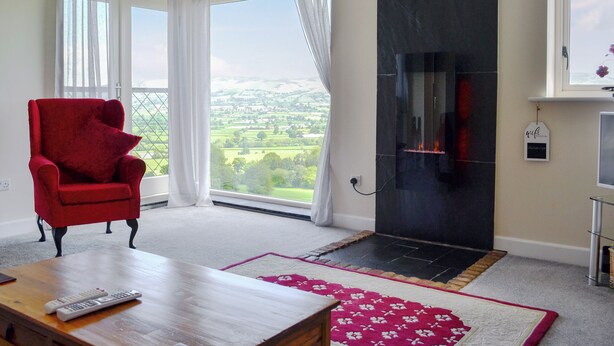A living room with a red armchair, a fireplace, a view of the countryside, and a wooden coffee table. - 2 bedroom accommodation in Llanrhaeadr, near Denbigh (Llanrhaeadr, near Denbigh)