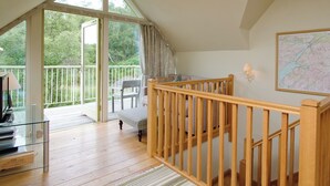 Une pièce spacieuse avec un escalier en bois, un balcon donnant sur un paysage verdoyant et une carte accrochée au mur.