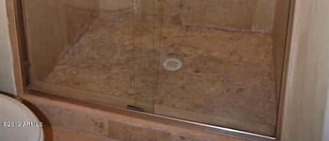 A glass-enclosed shower with a tiled floor, a handheld showerhead, and a handheld shower control.
