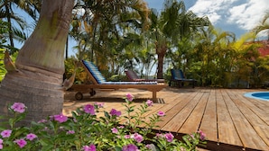 Une terrasse en bois avec des chaises longues, une piscine et des plantes tropicales.