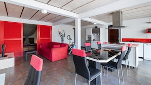 Une cuisine moderne dotée d’un îlot central, de touches de couleur rouge et d’un coin repas avec une table en verre et des chaises noires.