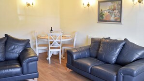 A living room with two black leather sofas, a round wooden table with chairs, and wall-mounted lighting. - 2 bedroom accommodation in Leyburn (Leyburn)