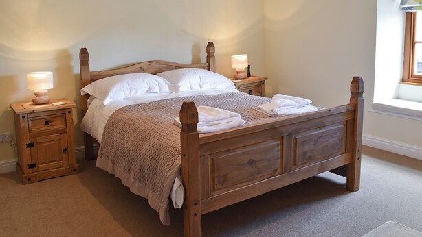 A wooden four-poster bed with white linens, two bedside tables with lamps, and a window with a view. - 2 bedroom accommodation in Leyburn (Leyburn)