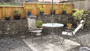 A patio with a round table and two chairs, a large umbrella, and several potted plants. - 2 bedroom accommodation in Leyburn (Leyburn)