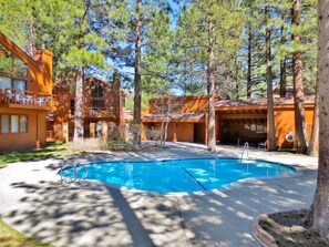 A pool area with a wooden deck, surrounded by trees and a building with a balcony. - Cozy, Spotless, Family Friendly - Walk to dining/shops, new remodeled bathrooms (Mammoth Lakes)