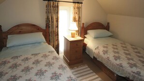 A bedroom with two wooden beds, a nightstand with a lamp, and a window with curtains. - Spring Cottage-E3846 (Kirk Ireton, near Matlock)